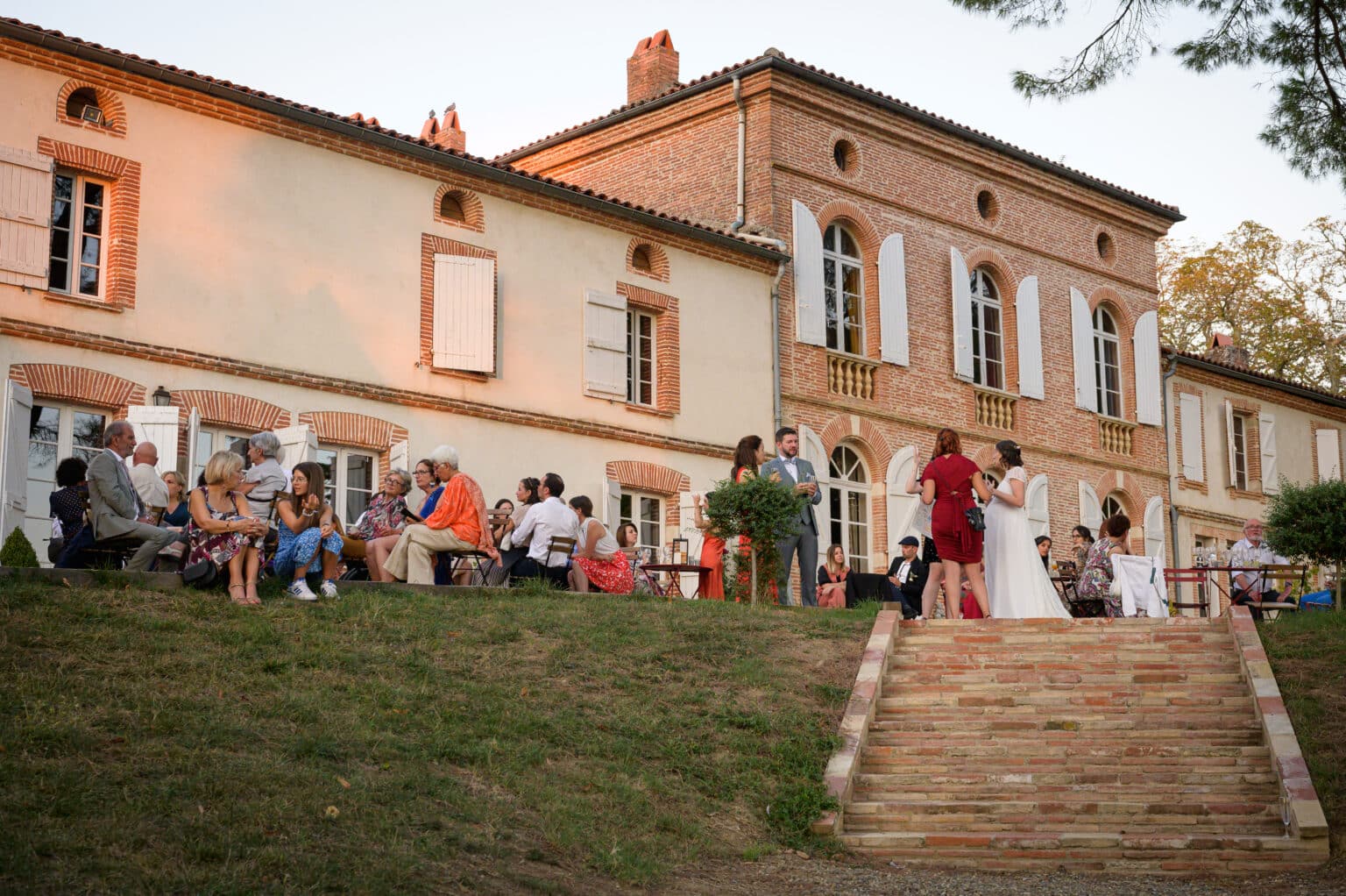 Invités discutant lors d’un cocktail de mariage devant un domaine en briques avec escaliers
