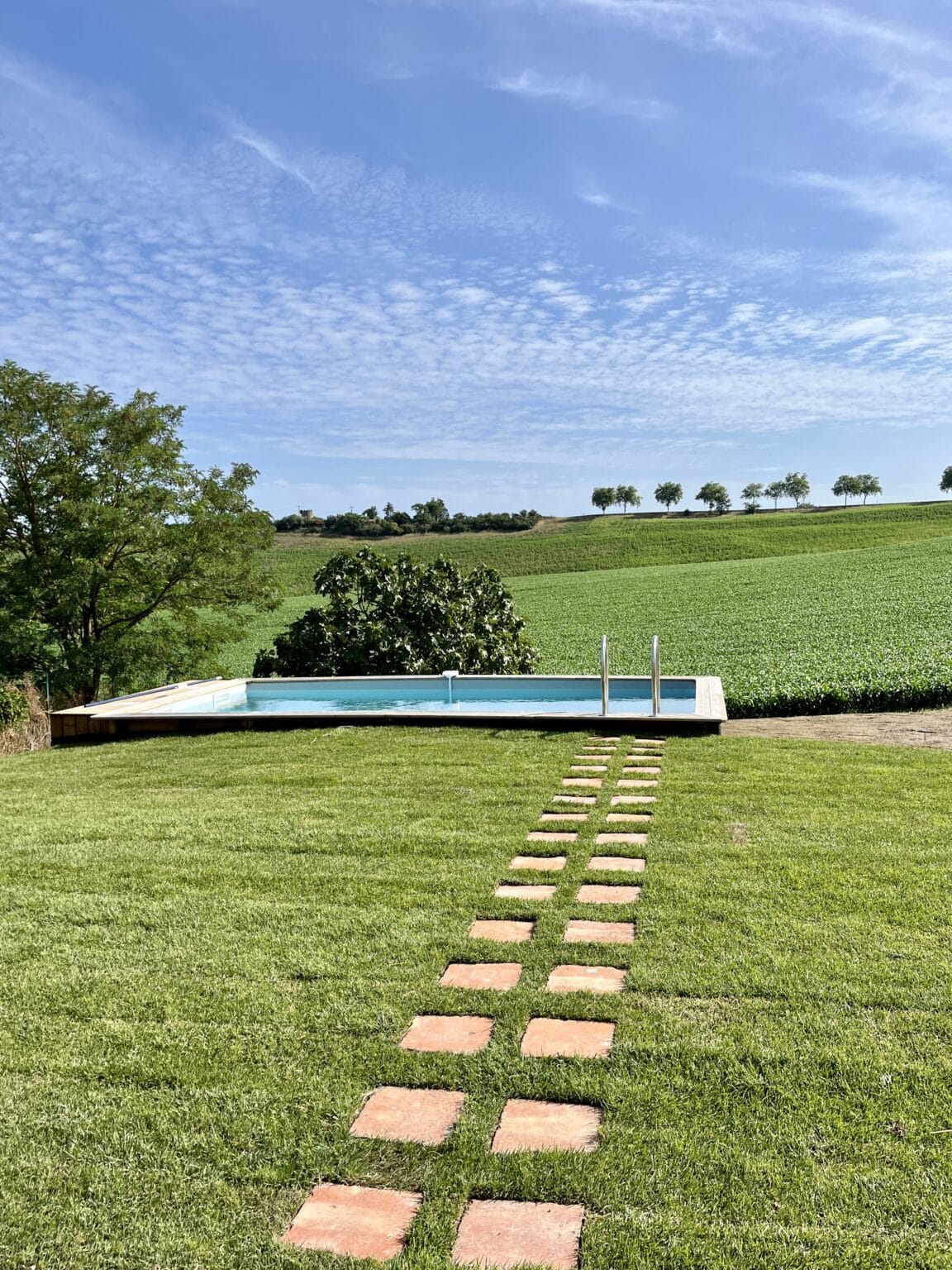 Piscine extérieure avec vue sur champs verdoyants et chemin en pierre dans le jardin d’un domaine