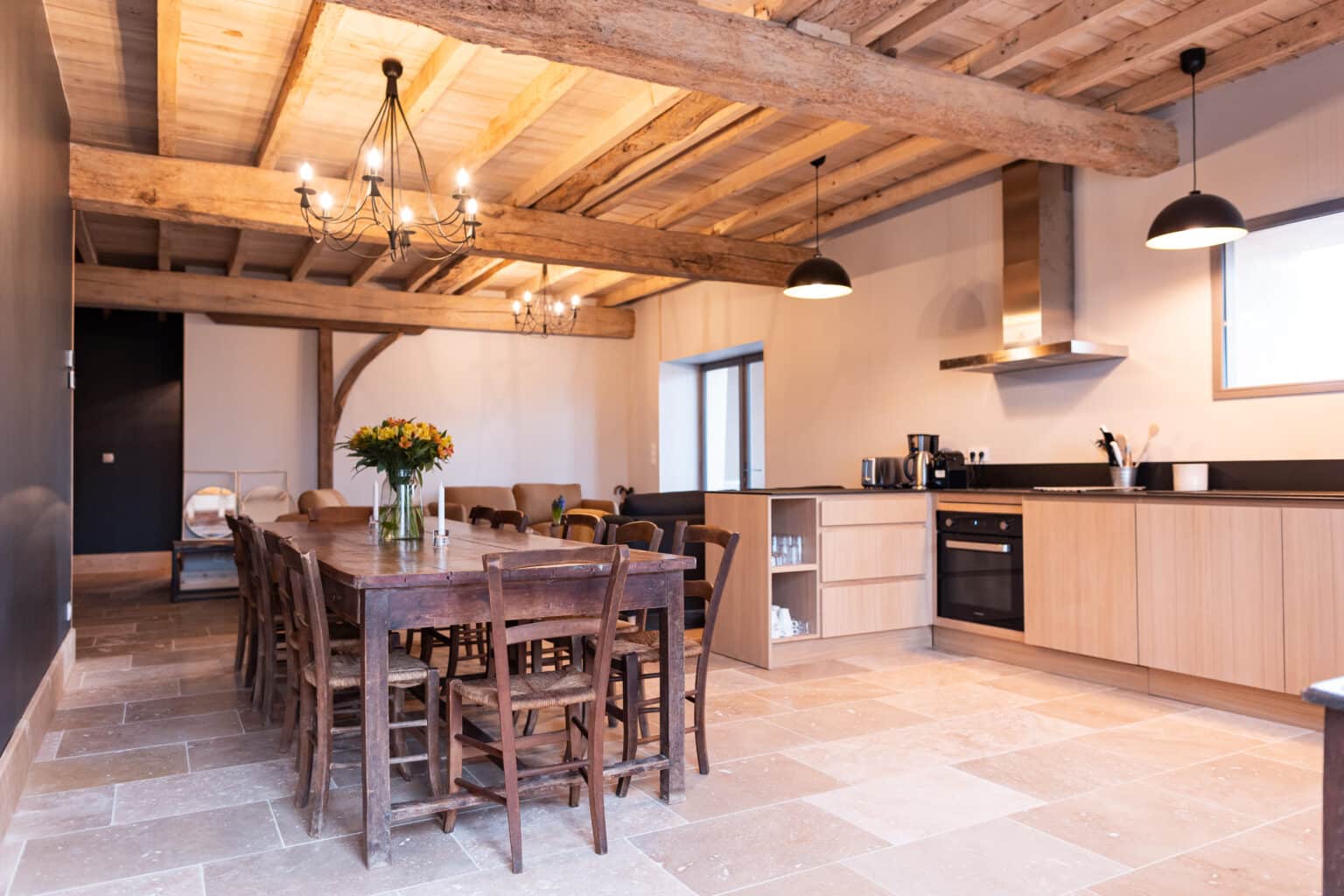 Grande salle de réception avec table en bois cuisine ouverte et poutres apparentes