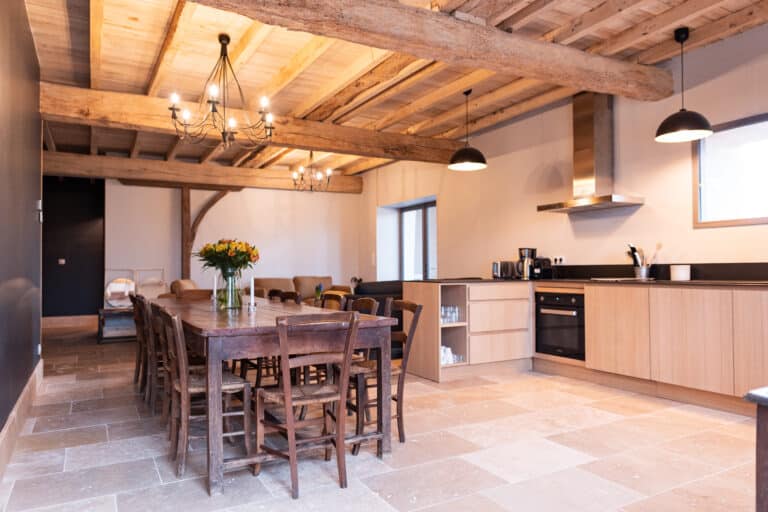 Grande salle de réception avec table en bois cuisine ouverte et poutres apparentes