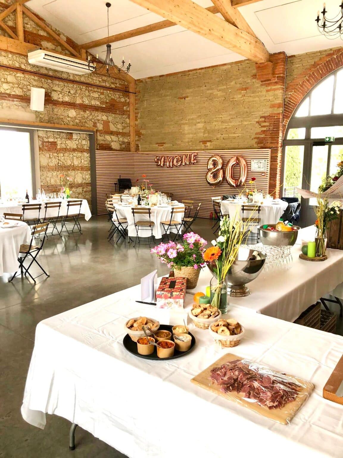 Salle de réception décorée pour un anniversaire 80 ans avec tables rondes buffet et ballons dorés