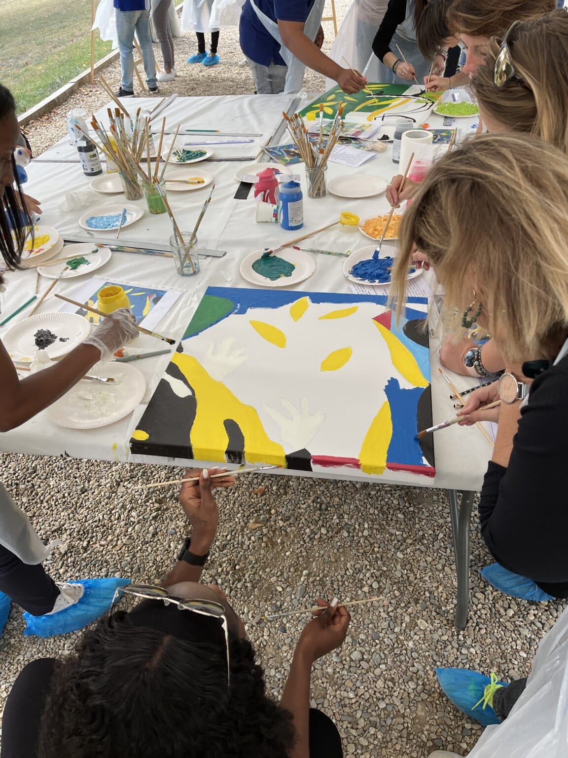 Participants en atelier team building réalisant une peinture collective sur toile avec pinceaux et peinture