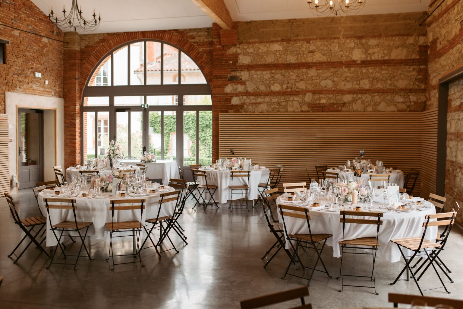Salle de réception pour mariage intimiste avec tables rondes décorées dans une grange rénovée