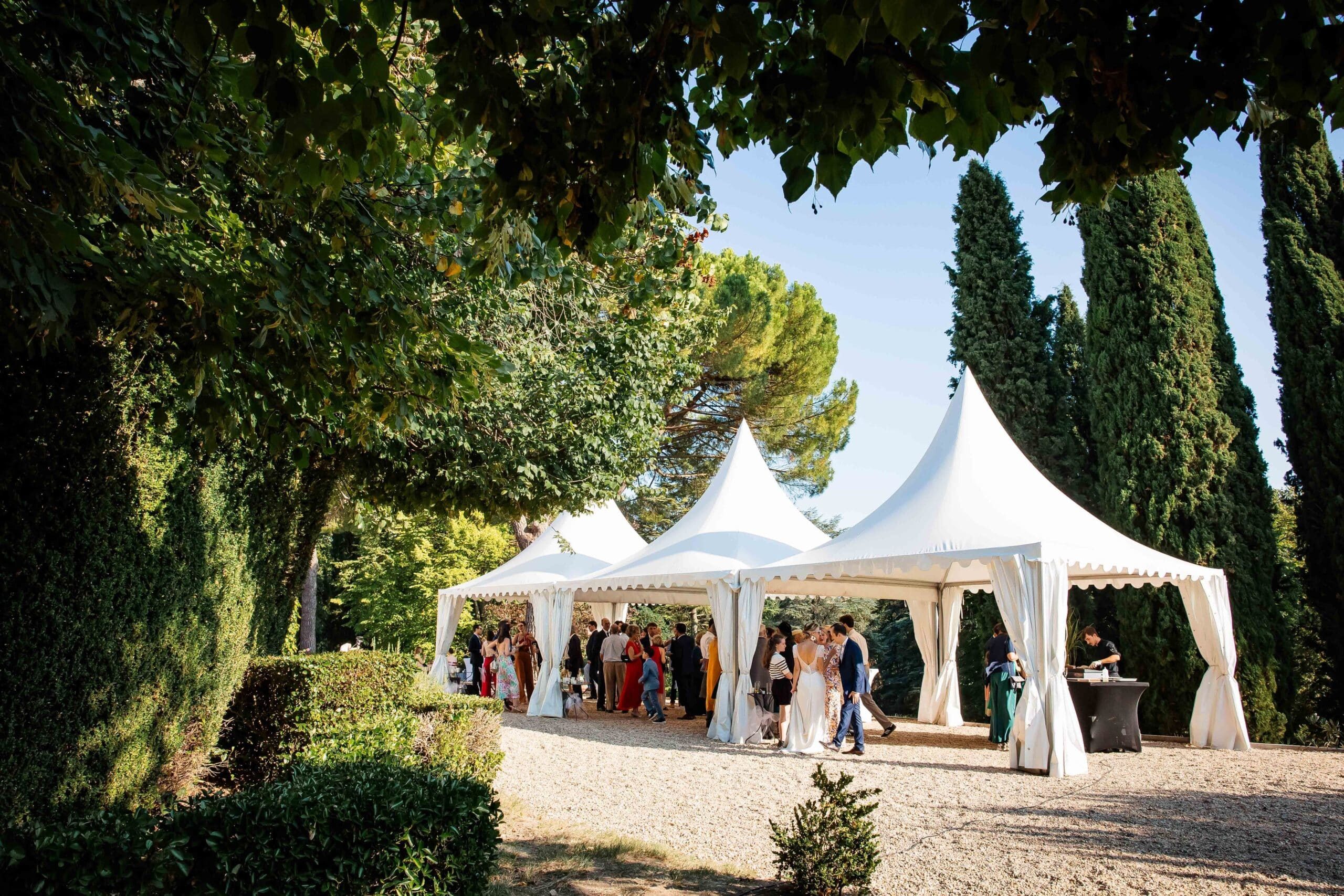 Invités réunis sous de grandes tentes blanches dans le jardin du domaine entouré de verdure